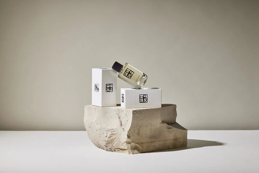 Ein edles Glasflakon mit einem Nischenduft der Marke Estoras auf einer Verpackung, auf einem Stein, angelehnt an eine zweite Verpackung