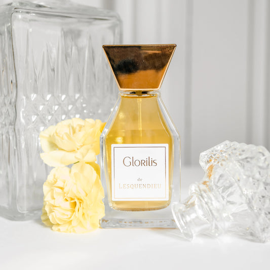 Das Flakon des exklusiven Nischenparfums Glorilis von der Marke Lesquendieu neben gelben Blumen und einem Glasgefaess