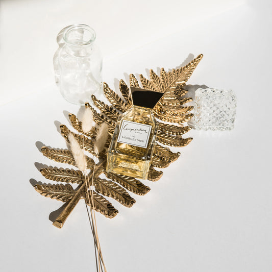 Das Flakon des exklusiven Nischenparfums le lesquendieu von der Marke Lesquendieu auf einem goldenen Farnblatt neben einem Glas