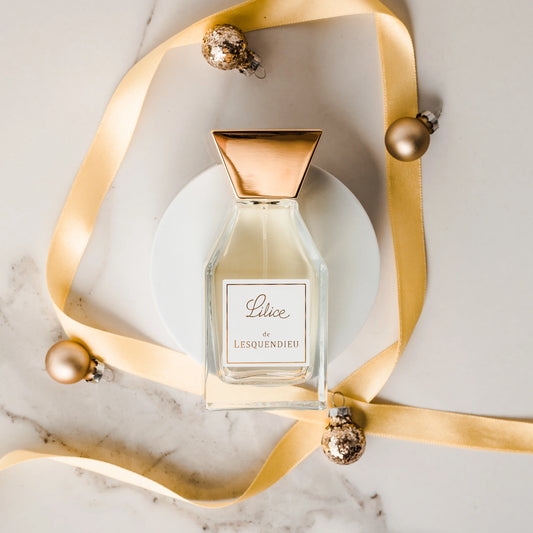 Das Flakon des exklusiven Nischenparfums Lilice von der Marke Lesquendieu mit einer grossen goldenen Schliefe auf einem weissen Marmoruntergrund