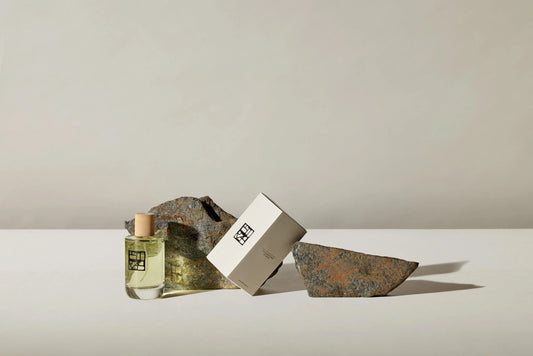 Eine 100ml Flasche mit Verpackung der Marke Estoras, mit Holzdeckel auf dem Glasflakon an 2 Steine angelehnt