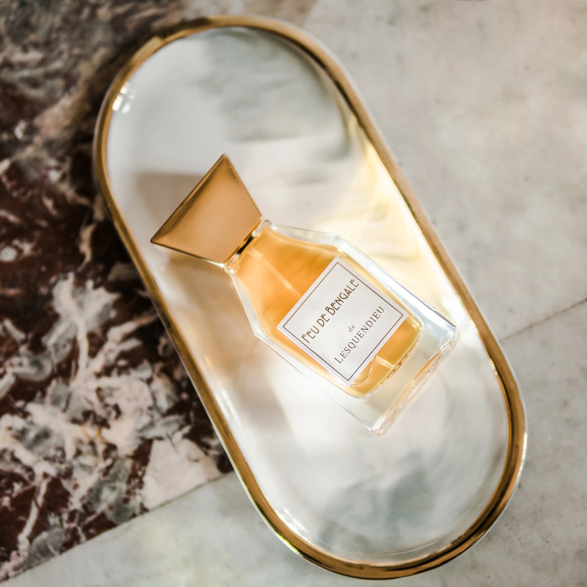 Das Flakon des exklusiven Nischenparfums Feu de Bengale von der Marke Lesquendieu auf einem goldenen Farnblatt auf einem Spiegel
